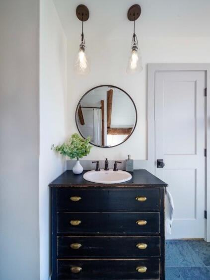 A chest of drawers converted to a vanity with vintage pendant lighting above.
